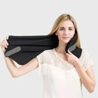 A woman wearing a white lace top holds up a black neck support pillow with gray padding against a light gray background.