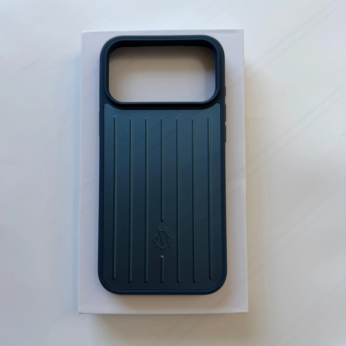 A dark teal phone case with a vertical ribbed design and a large camera cutout, displayed on top of its white packaging box against a light gray background.