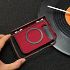 A hand holds a red textured phone case with a black circular ring and dark patterned border, placed over a vinyl record on a dark surface.