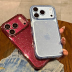 Two glittery phone cases held in a hand over a wooden table. One case is metallic rose gold/magenta and the other is light blue.