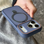 A navy blue protective phone case with a built-in magnetic ring and kickstand, shown being held by a hand over gray clothing.