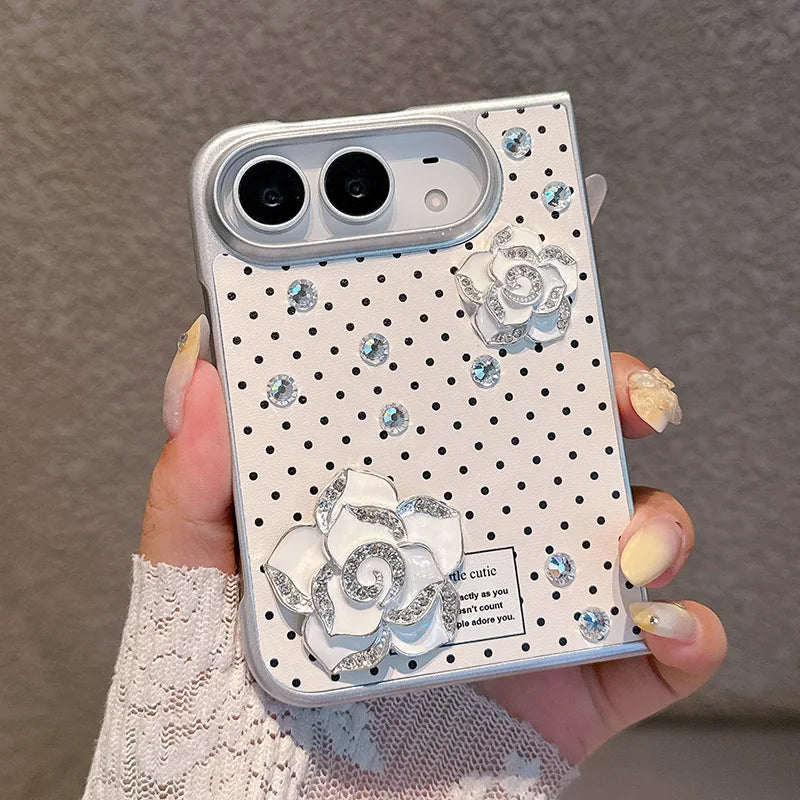 A hand holding a white phone case decorated with black polka dots, rhinestone flowers, and small clear rhinestones, shown against a neutral gray background.