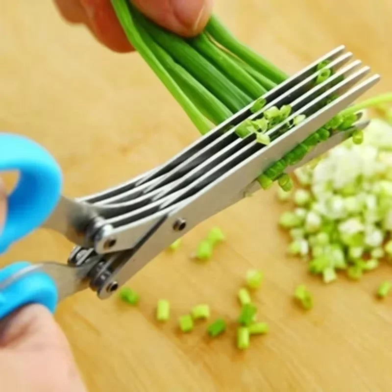 Close-up of a hand using a pair of kitchen shears with blue handles to chop green scallions on a wooden cutting board.