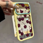 A hand holding a pastel yellow phone case with a transparent back panel printed with dark red cherries, featuring a light blue camera bumper and a matching translucent inner bumper.