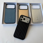 Three slim protective phone cases with vertical ridges are displayed in their white retail boxes, with one black case placed in front. The cases come in dark blue, metallic gold, and metallic silver colorways.
