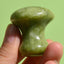 green quartz facial roller mushroom massager held between fingers for eye depuffing and facial massage