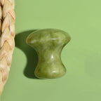 green quartz facial roller mushroom massage tool on green background for skin care and neck relaxation