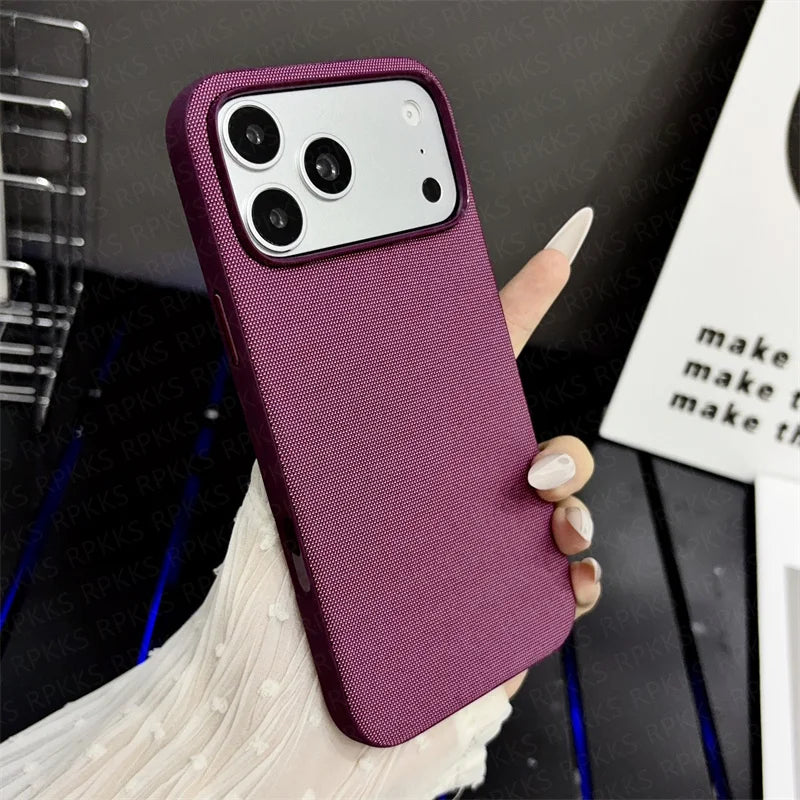 A hand holding a purple textured phone case with a silver camera surround, shown against a dark desk background with a white card. Main image
