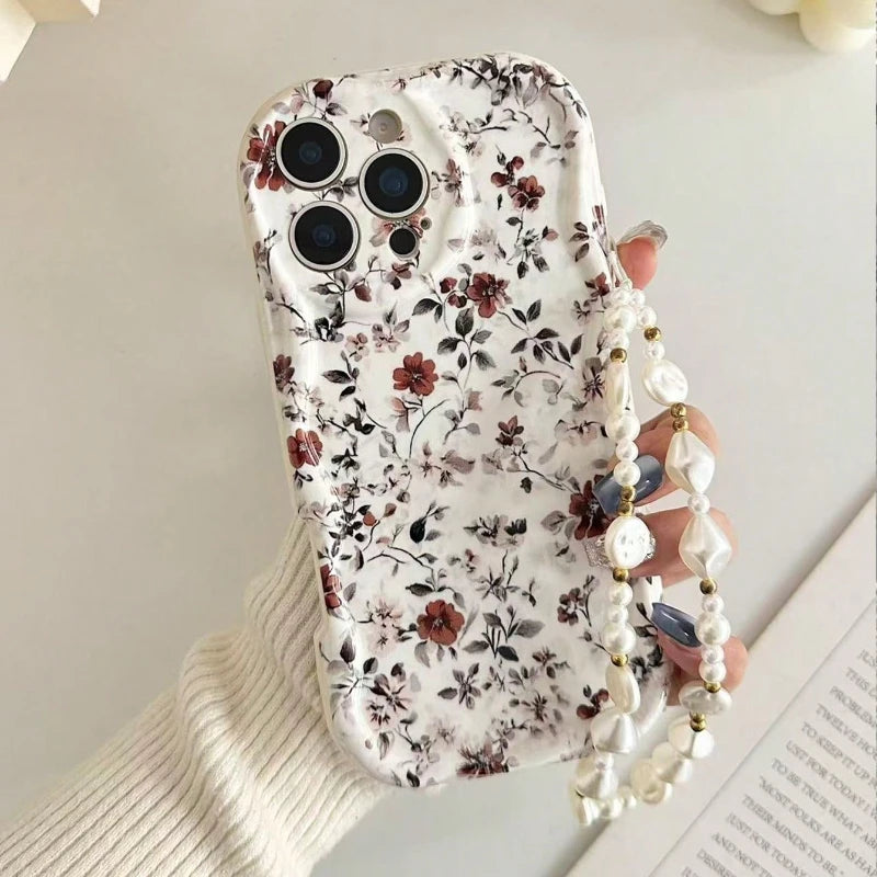 A hand holding a white phone case decorated with a delicate red and black floral pattern, featuring a pearl-bead wrist strap.