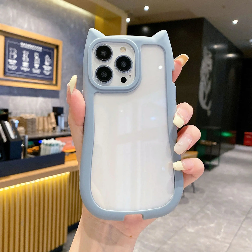 A hand holding a light blue cat-ear phone case with a frosted white back panel, shown in a cafe setting.