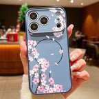 A hand holding a blue phone case decorated with pink cherry blossom branches and flowers, set against a blurred indoor background.