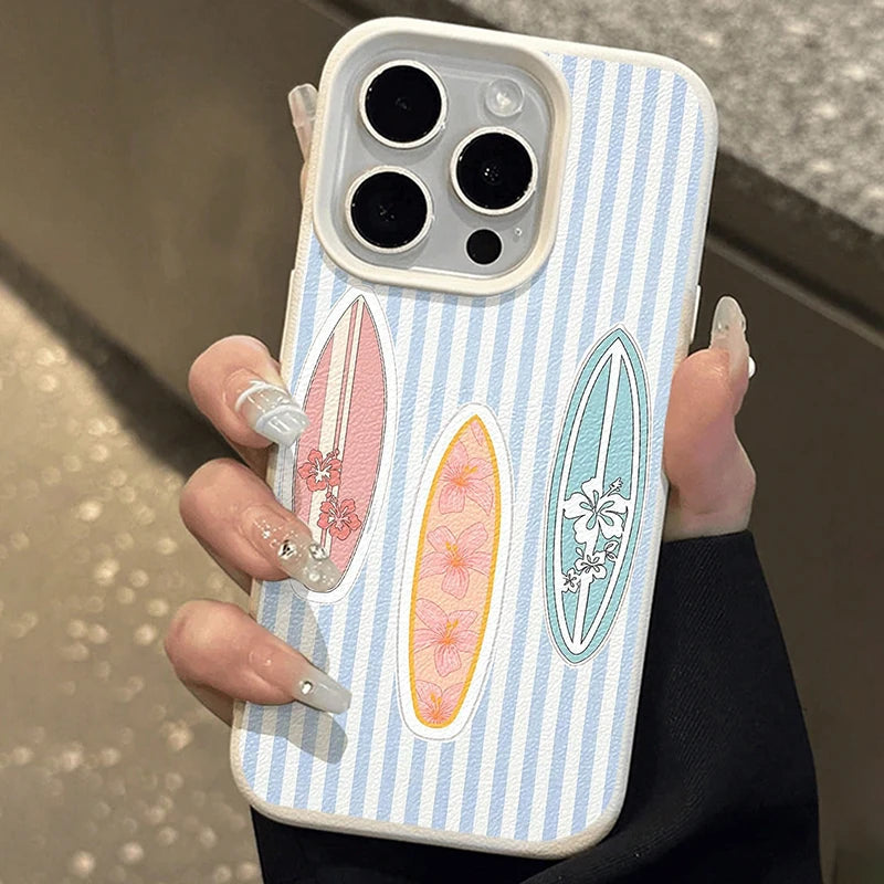 A hand with long decorated nails holds a light blue and white striped phone case featuring three vertical surfboard designs with pink, peach, and mint floral patterns.