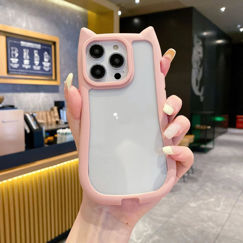 A hand holding a light pink cat-ear phone case with a frosted back panel, shown in a cafe setting.