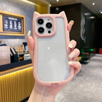 A hand holding a light pink cat-ear phone case with a frosted back panel, shown in a cafe setting.