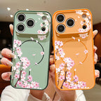 Two phone cases held in hands, one sage green and one orange, both decorated with pink cherry blossom branches and a black circular graphic.