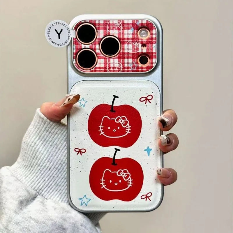 A hand holding a phone case featuring a white background with two red apple graphics and small bow and star accents, plus a red-and-white gingham camera cutout area. The hand is wearing a light gray ribbed sweater.