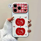 A hand holding a phone case featuring a white background with two red apple graphics and small bow and star accents, plus a red-and-white gingham camera cutout area. The hand is wearing a light gray ribbed sweater.