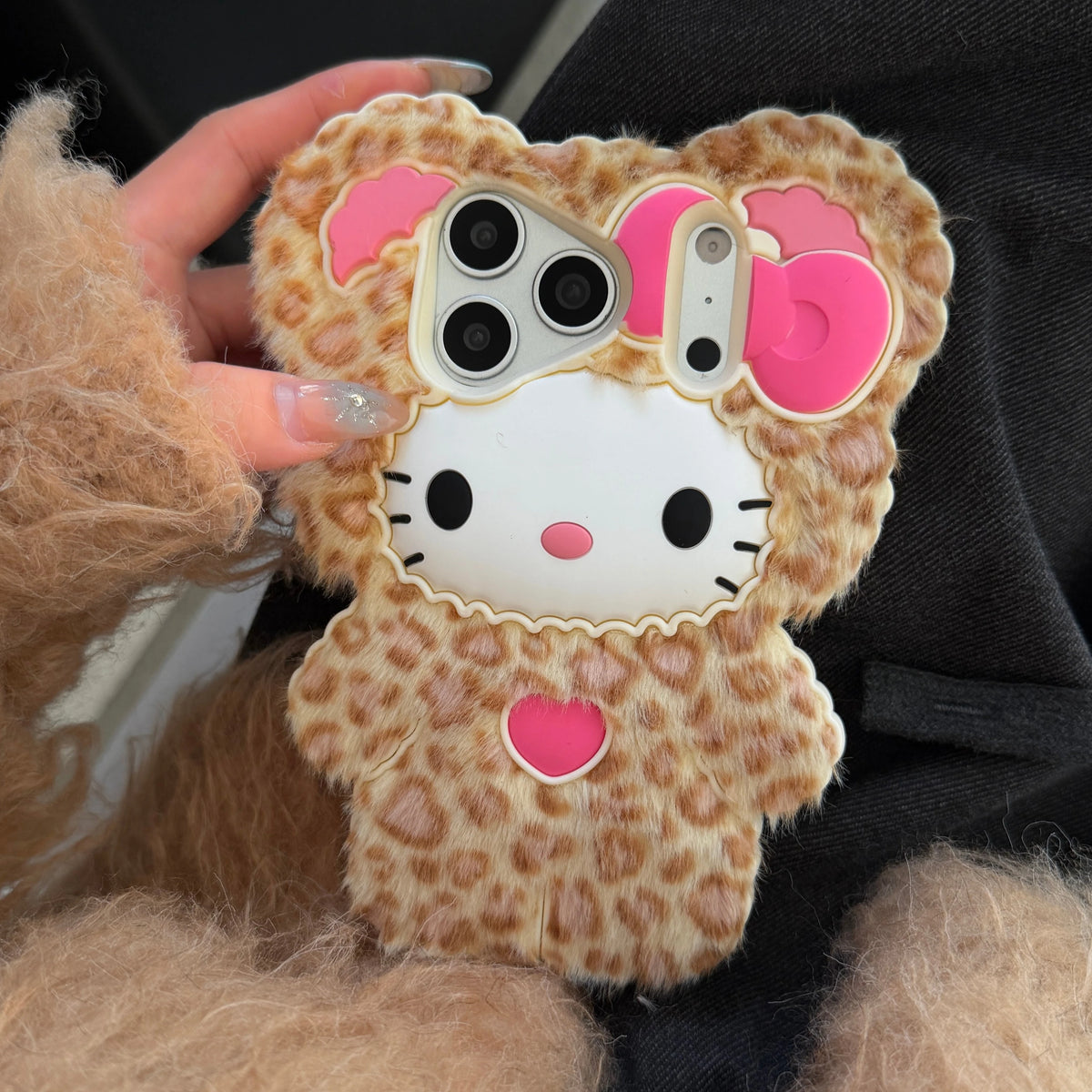 Phone case with leopard print and pink bow held by a person wearing a fuzzy brown sleeve.