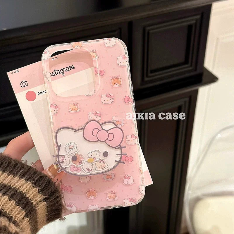 A hand holds a pink Hello Kitty phone case with a large Hello Kitty face graphic and small pastel character prints. The case is shown in a real indoor setting with a dark cabinet in the background, and a card with the text 'akia case' is visible.