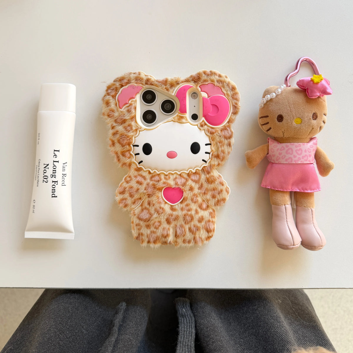 Phone case with leopard print and Hello Kitty design, next to a plush toy and skincare product.