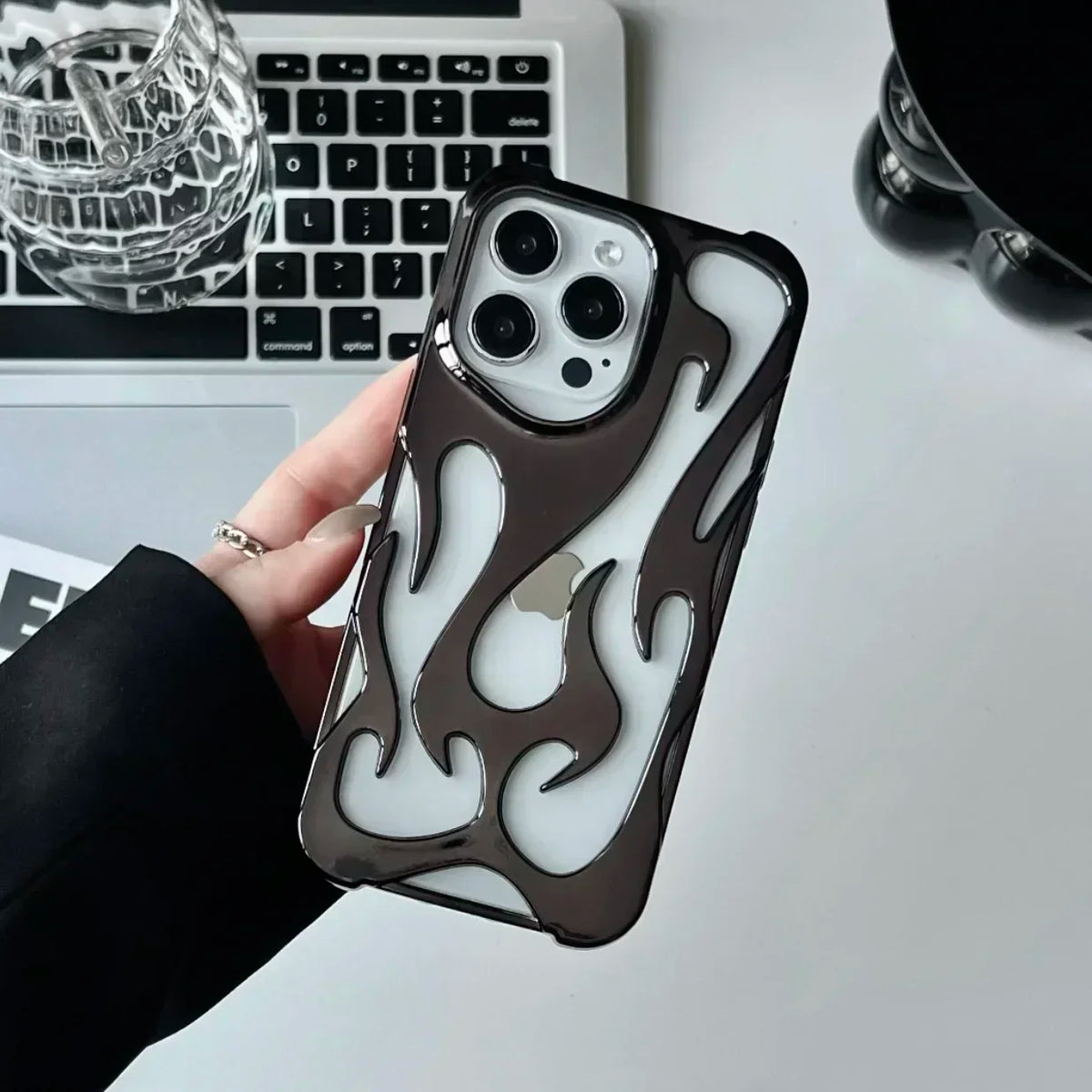 Person holding a phone with a flame design case in front of a laptop.