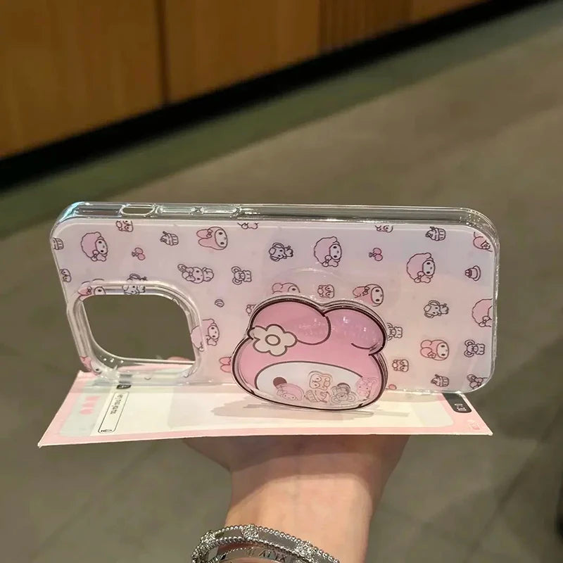 A clear phone case with a pink and white My Melody pattern, held in a hand. The case features a large pink My Melody character graphic on the back and a built-in pop socket.