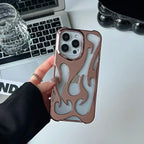 Phone case with flame design held by a hand, laptop and glass in the background
