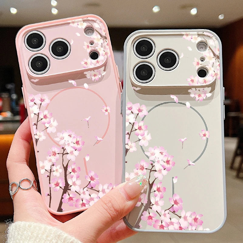 Two iPhone cases held in a hand, one in pastel pink and one in pastel white, both decorated with cherry blossom branches and flowers.