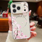 A hand holding a clear phone case with a pink cherry blossom branch pattern, shown against a blurred indoor background.