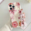 A hand wearing a white ribbed knit sleeve holds a phone case decorated with pink and red hibiscus flowers on a cream background. The case has a clear beaded wrist strap with pink flower charms.
