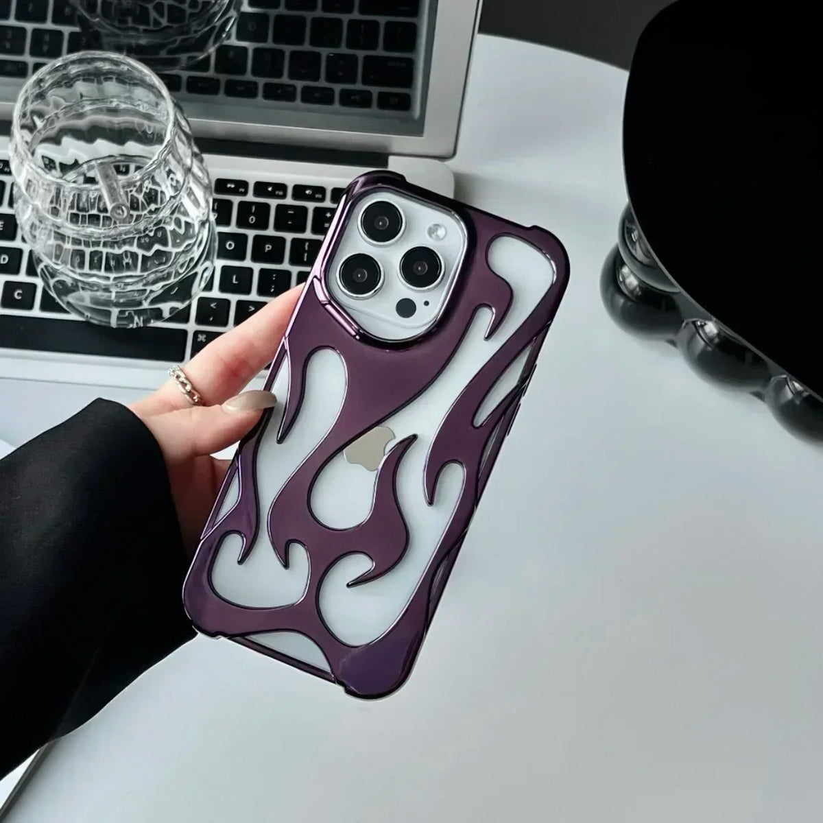 Person holding a phone with a flame design case on a desk with a laptop and glassware.