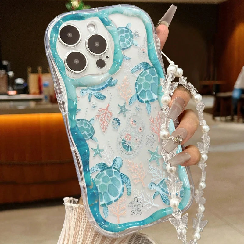 Phone case with turtle design held by a hand with a pearl bracelet.