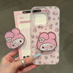 A hand holds a pink My Melody phone case with a matching 3D pop-spring accessory. The phone case has a light pink background with a repeating pattern of My Melody cartoon characters, and the matching accessory features a large pink My Melody head with a white flower and small character details.