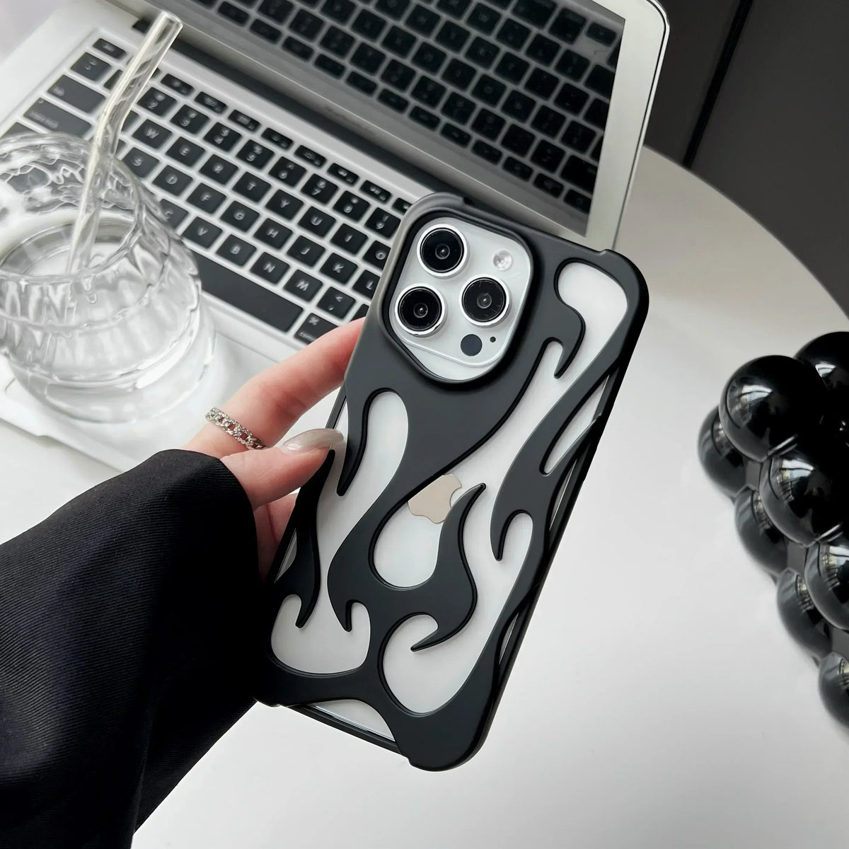 Person holding a phone with a black and white flame-patterned case in front of a laptop.