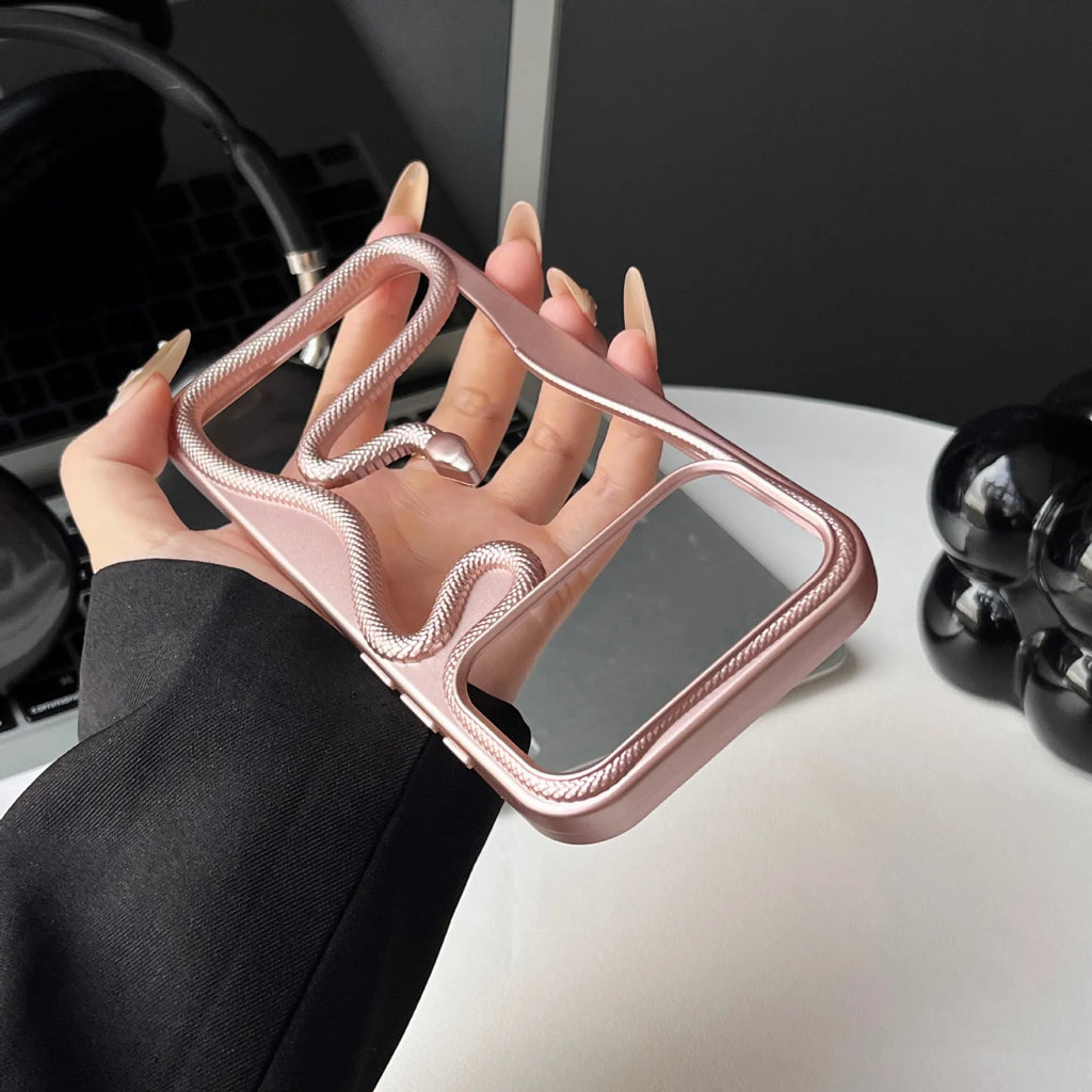 A hand holding a rose gold phone case with a textured snake-like strap detail and a mirrored camera lens protector, set against a modern desk background.
