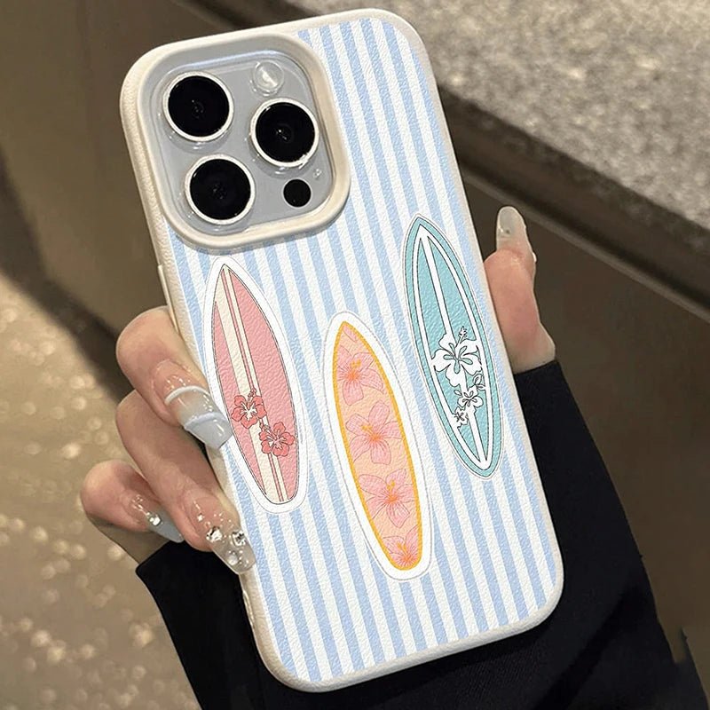 A hand holding a light blue and white striped phone case decorated with three colorful surfboard designs, shown against an indoor background.