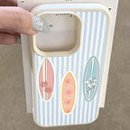 A hand with glittery fingernails holds a phone case featuring a light blue and white vertical stripe pattern with three surfboard designs in pink, orange, and blue.