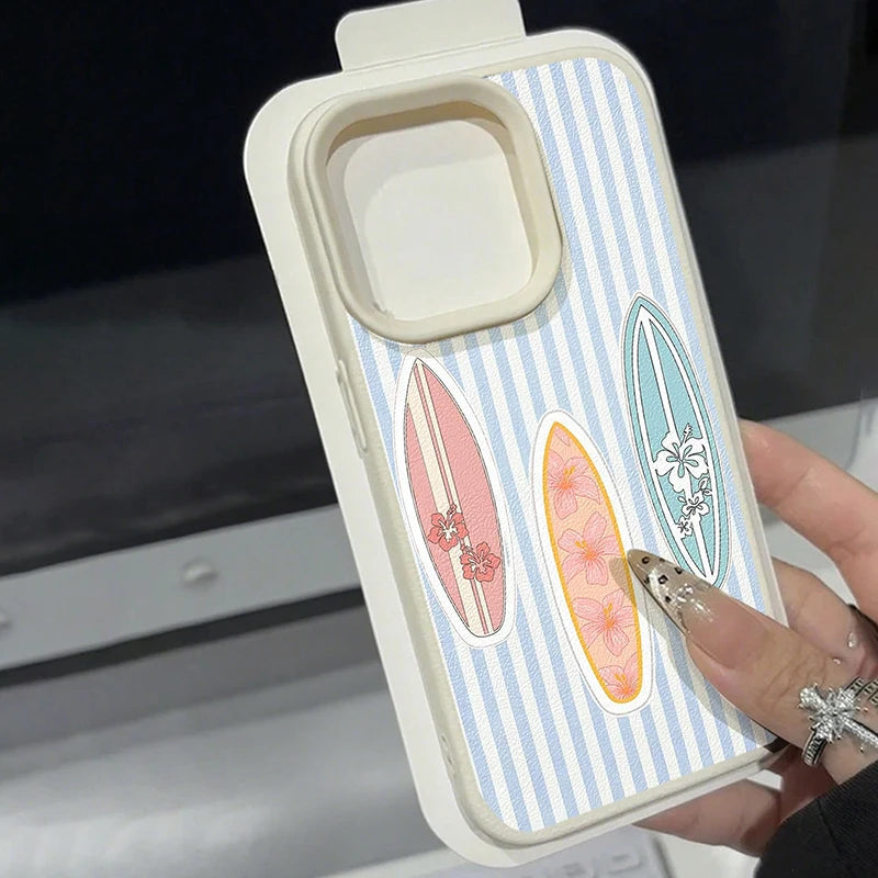 A hand holding a phone case with a light blue and white vertical stripe pattern, decorated with three retro surfboard stickers in pink, orange, and teal. The case has a cream-colored bumper and a large camera cutout.