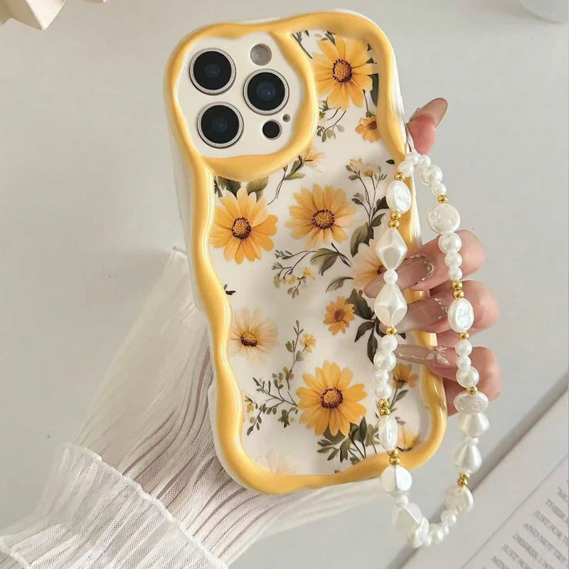 A hand holding a phone with a floral yellow and white phone case featuring a pearl strap, set against a light background.