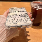 A hand holding a clear phone case featuring black line art illustrations of Simba and Nala from Disney's The Lion King, with the movie title printed above. The hand is resting on a wooden table next to an iced coffee.