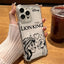 A hand holds a clear phone case featuring black printed artwork of Simba and Nala with the text 'THE LION KING' and a Disney logo. The case is shown on a phone over a wooden table, with an iced coffee cup in the background.