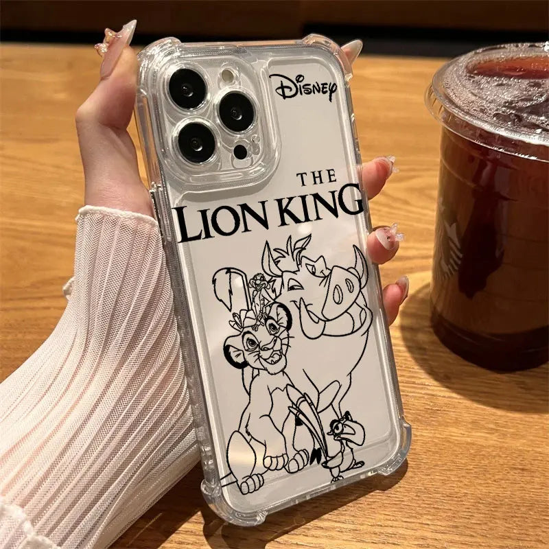 A hand wearing a ribbed cream sweater holds a clear iPhone case featuring black line art of The Lion King characters and the Disney logo. The photo is taken on a wooden table next to an iced coffee.