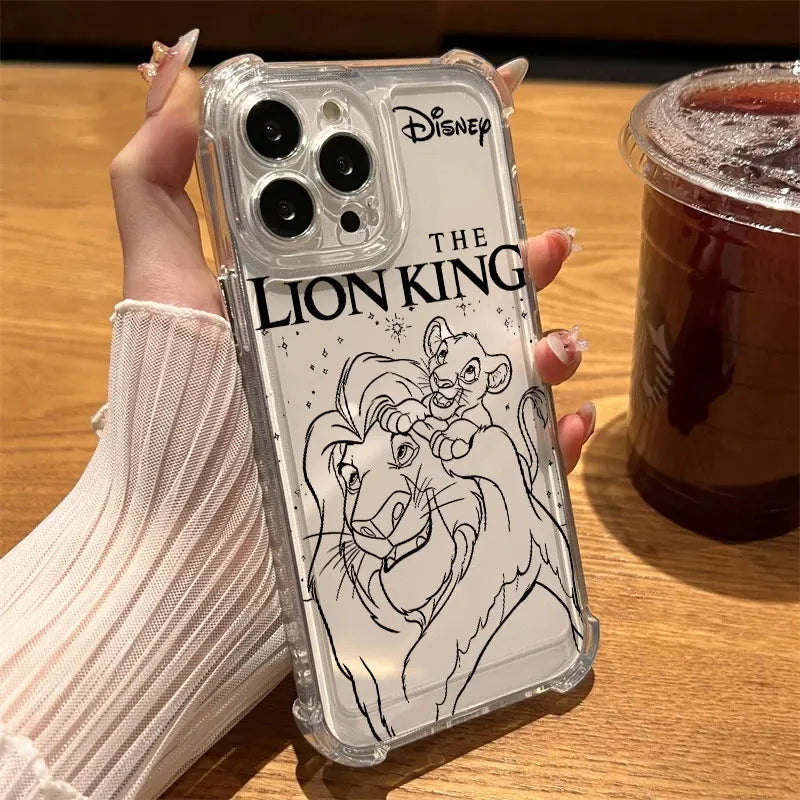 A hand wearing a ribbed cream sweater holds a clear phone case featuring black line art of Simba and Nala from Disney The Lion King, with the Disney logo and 'THE LION KING' text on the back. The phone case is shown over a smartphone, with a wooden table and an iced coffee cup in the background.