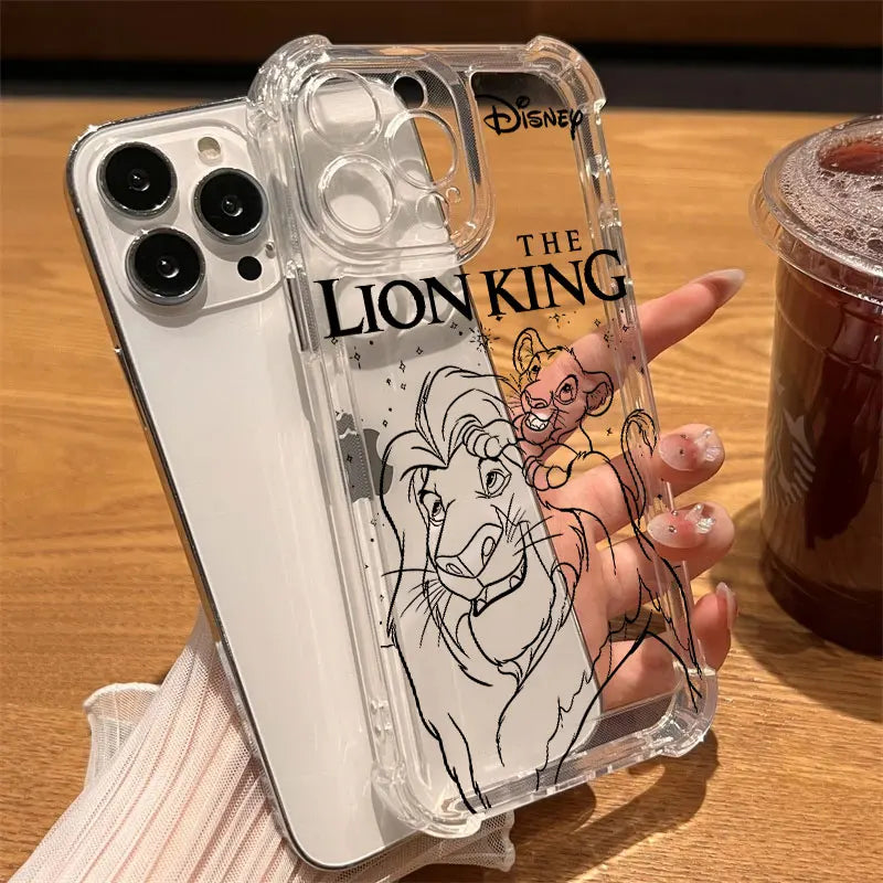 A hand holds a clear iPhone case featuring black line art of Simba and Nala with 'THE LION KING' text and a Disney logo, shown over a white iPhone on a wooden table next to an iced coffee.