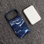 A phone case with a blue and white ocean wave pattern, shown next to a white rectangular power bank on a textured gray carpet.
