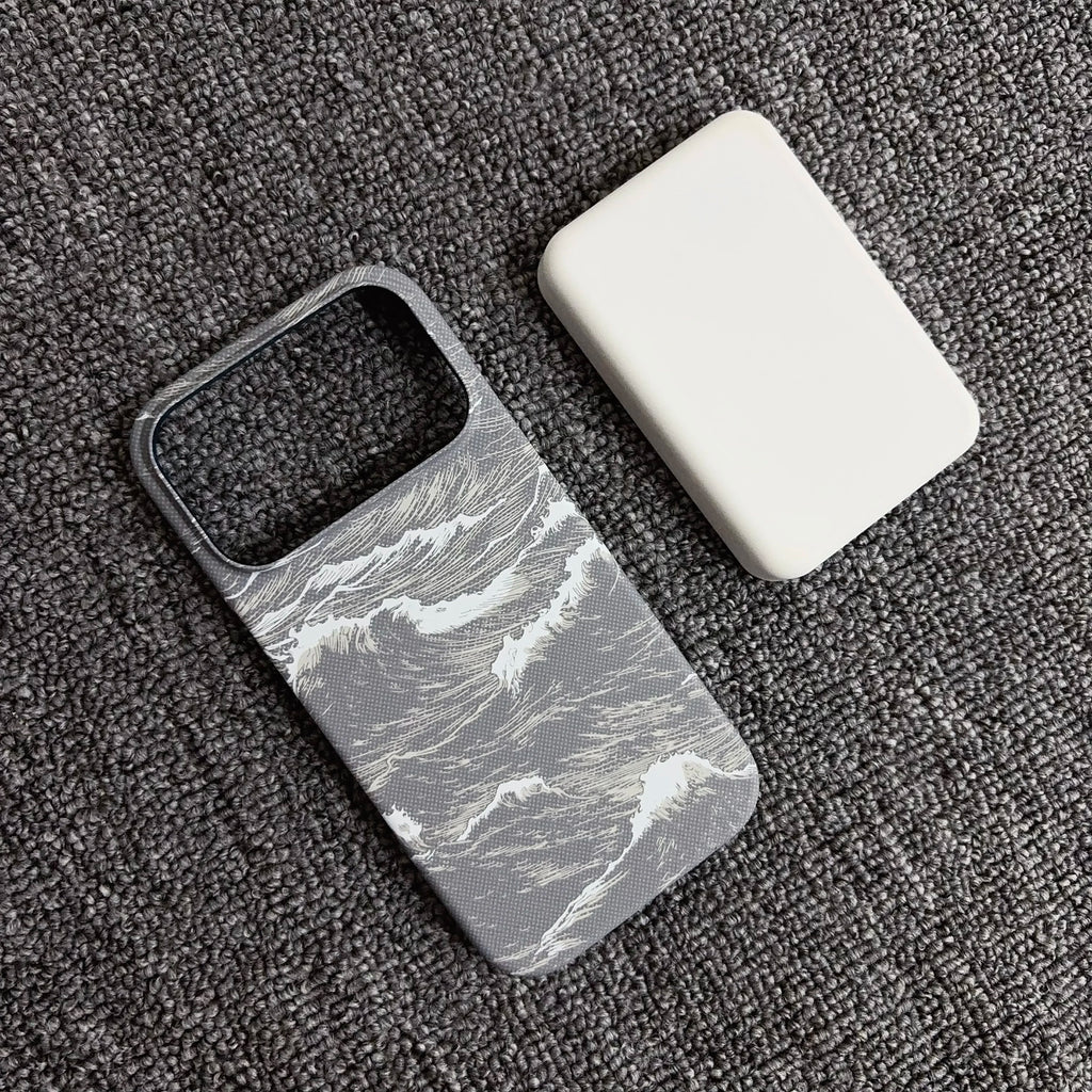 A gray and white ocean wave pattern phone case next to a plain white rectangular protective cover, displayed on a dark gray textured fabric background.