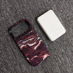 A phone case with a dark red and black marble wave pattern, shown next to a white rectangular protective cover on a textured gray carpet.