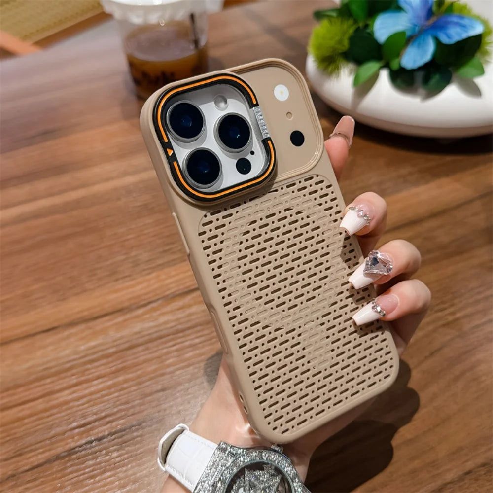 A hand holding a beige textured phone case with a raised camera bumper and orange accent ring, photographed over a wooden table with blurred background decor.
