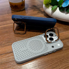 Two smartphone cases on a wooden table: a light gray case in the foreground with a raised orange ring stand, and a dark blue case in the background with a matching stand.