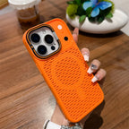 A hand with decorated nails holds an orange textured phone case with a circular speaker grille design, shown on a wooden table background.